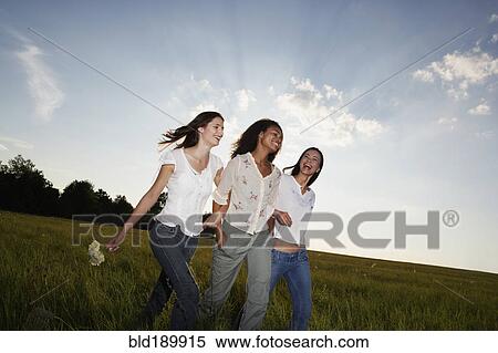 Stock Photography - Three women walking arm in arm through meadow. Fotosearch