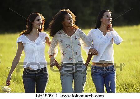 Stock Image - Three women walking through meadow. Fotosearch