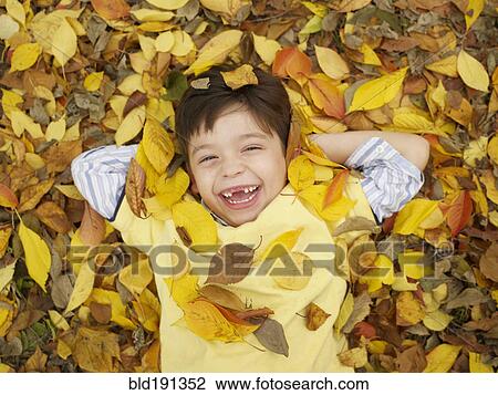 Stock Image - Toothless Hispanic boy laying in autumn leaves. Fotosearch