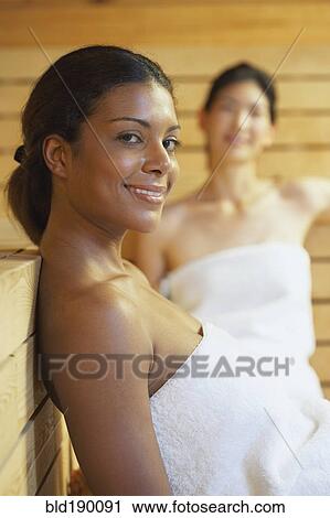 Stock Image - Two multi-ethnic women relaxing in sauna. Fotosearch