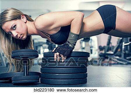 Stock Image - Woman doing push-ups on weightlifting plates in gym. Fotosearch