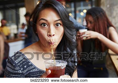 Stock Image - Woman drinking cold drink with straw in cafe. Fotosearch