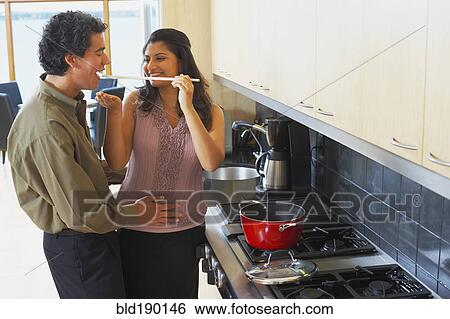 Stock Photograph - Woman feeding husband in kitchen. Fotosearch