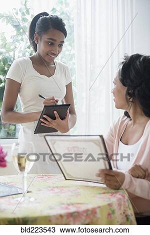Stock Image - Woman holding menu ordering in restaurant. Fotosearch