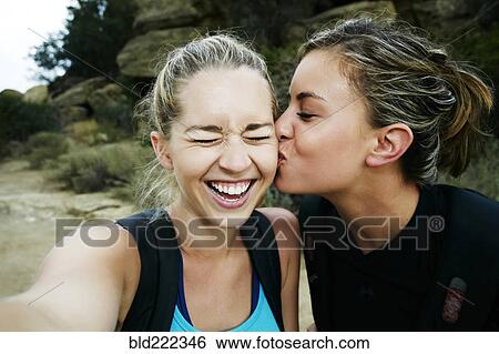 Stock Photograph - Woman kissing cheek of friend outdoors. Fotosearch