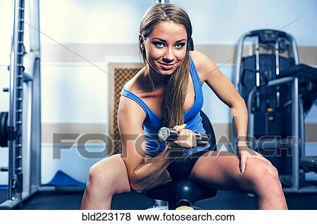 Stock Photo - Woman lifting dumbbells in gym. Fotosearch