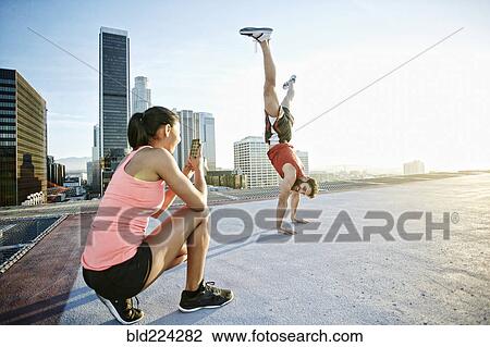 Woman photographing man doing handstand on urban rooftop View Large Photo Image Stock Image - Woman photographing man doing handstand on urban rooftop. Fotosearch