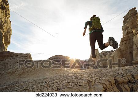 Stock Image - Woman running in canyon wearing backpack. Fotosearch