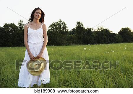 Stock Photo - Woman standing in meadow holding straw hat. Fotosearch