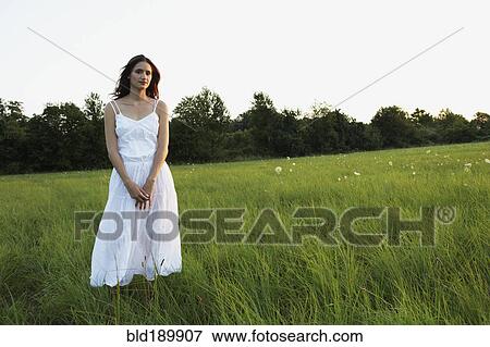 Stock Photo - Woman standing in meadow with hands clasped. Fotosearch