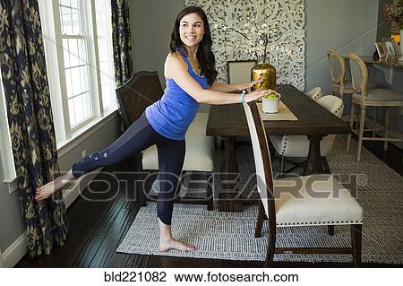 Stock Image - Woman stretching in dining room. Fotosearch