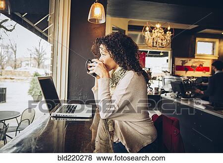 Stock Photo - Woman using laptop and drinking coffee in cafe. Fotosearch