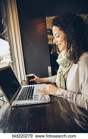 Stock Photo - Woman using laptop and drinking coffee in cafe. Fotosearch