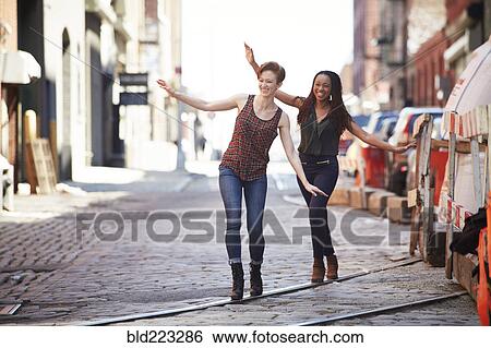 Stock Photograph - Women balancing on track in cobblestone city street. Fotosearch
