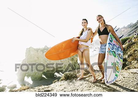 Stock Photo - Women carrying surfboards at beach. Fotosearch