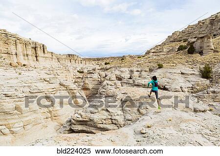 Stock Photography - Women jumping to rock in canyon wearing backpack. Fotosearch