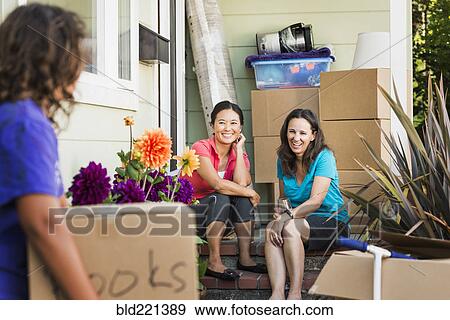 Stock Photo - Women moving cardboard boxes into house. Fotosearch