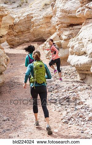 Picture - Women running in canyon wearing backpacks. Fotosearch