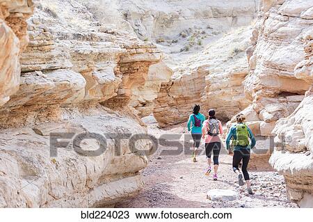 Stock Image - Women running in canyon wearing backpacks. Fotosearch