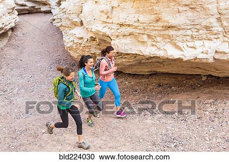 Stock Image - Women running in canyon wearing backpacks. Fotosearch