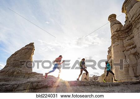 Stock Image - Women running in canyon wearing backpacks. Fotosearch