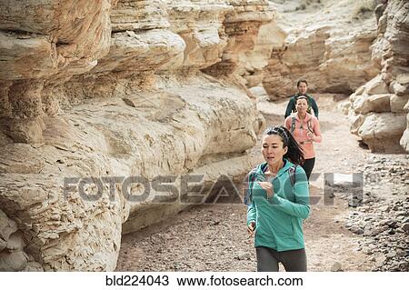 Stock Image - Women running in canyon wearing backpacks. Fotosearch