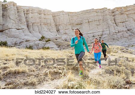 Stock Photo - Women running in canyon wearing backpacks. Fotosearch