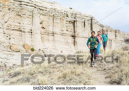 Stock Photograph - Women running in canyon wearing backpacks. Fotosearch