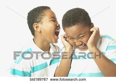 Stock Photo - Young African boy yelling into twin brother's ear. Fotosearch