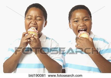 Stock Image - Young African twin brothers eating cupcakes. Fotosearch