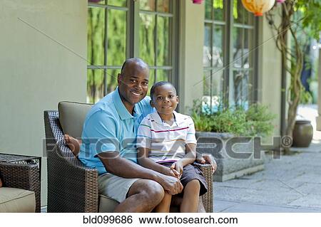 Stock Photograph - African American father and son sitting on patio. Fotosearch