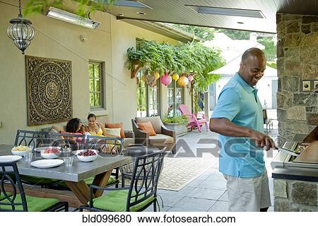 Stock Image - African American man grilling food on barbecue. Fotosearch