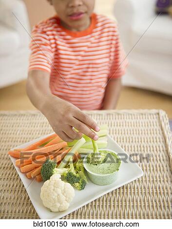 Stock Image - Black boy eating vegetables and dip. Fotosearch