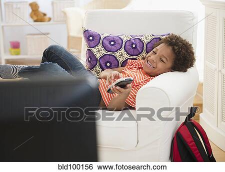 Stock Photograph - Black boy laying in chair watching television. Fotosearch