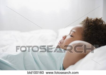 Stock Image - Black boy laying on bed. Fotosearch