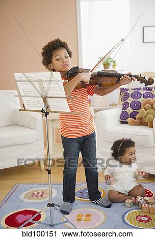 Stock Image - Black boy practicing violin in living room. Fotosearch