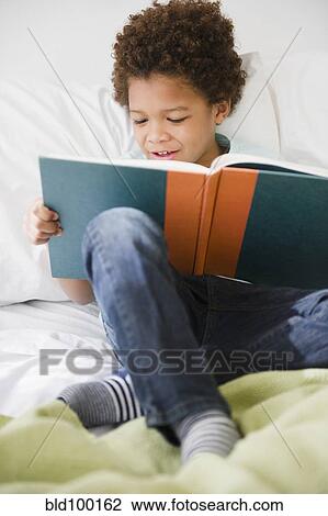 Stock Image - Black boy reading book in bed. Fotosearch