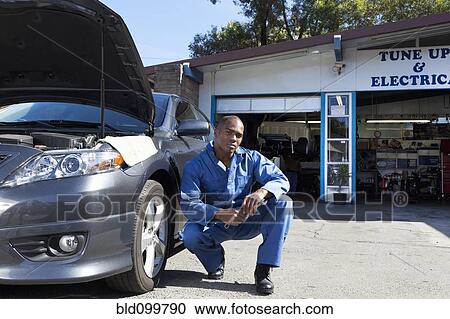 Stock Image - Black mechanic squatting near car. Fotosearch