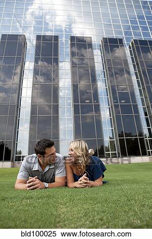 Stock Photography - Caucasian couple laying together in grass near building. Fotosearch