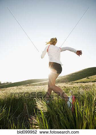 Stock Image - Caucasian woman running in remote field. Fotosearch