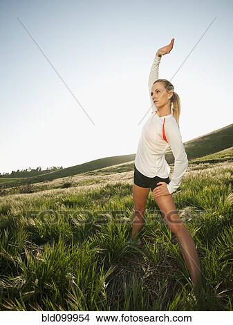 Picture - Caucasian woman stretching in remote field. Fotosearch