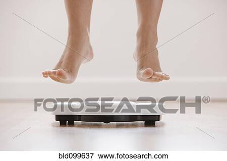 Stock Photo - Caucasian woman's feet jumping on scale. Fotosearch