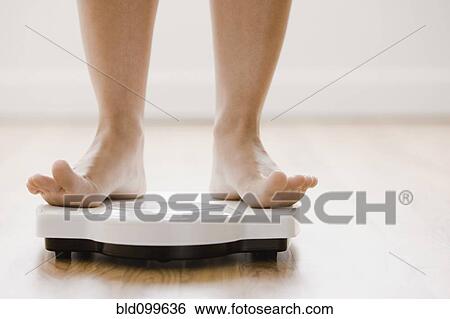 Stock Photograph - Caucasian woman's feet standing on scale. Fotosearch