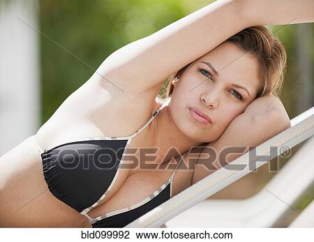 Stock Image - Colombian woman in bikini laying on lounge chair. Fotosearch