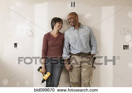 Stock Image - Couple holding hands in unfinished room. Fotosearch