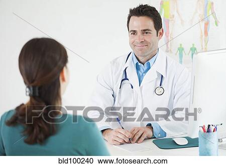 Stock Image - Doctor sitting at desk with patient. Fotosearch