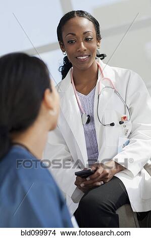 Picture - Doctor with cell phone talking to co-worker. Fotosearch