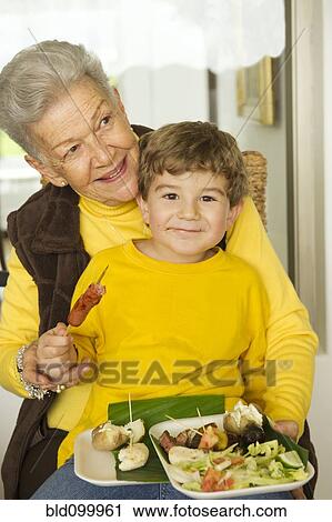 Hispanic boy eating while sitting on grandmother's lap View Large Photo Image Stock Image - Hispanic boy eating while sitting on grandmother's lap. Fotosearch