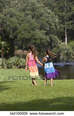 Stock Photo - Hispanic girls walking in park holding hands. Fotosearch