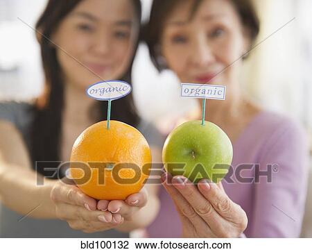 Stock Image - Japanese mother and daughter holding fruit with organic label. Fotosearch